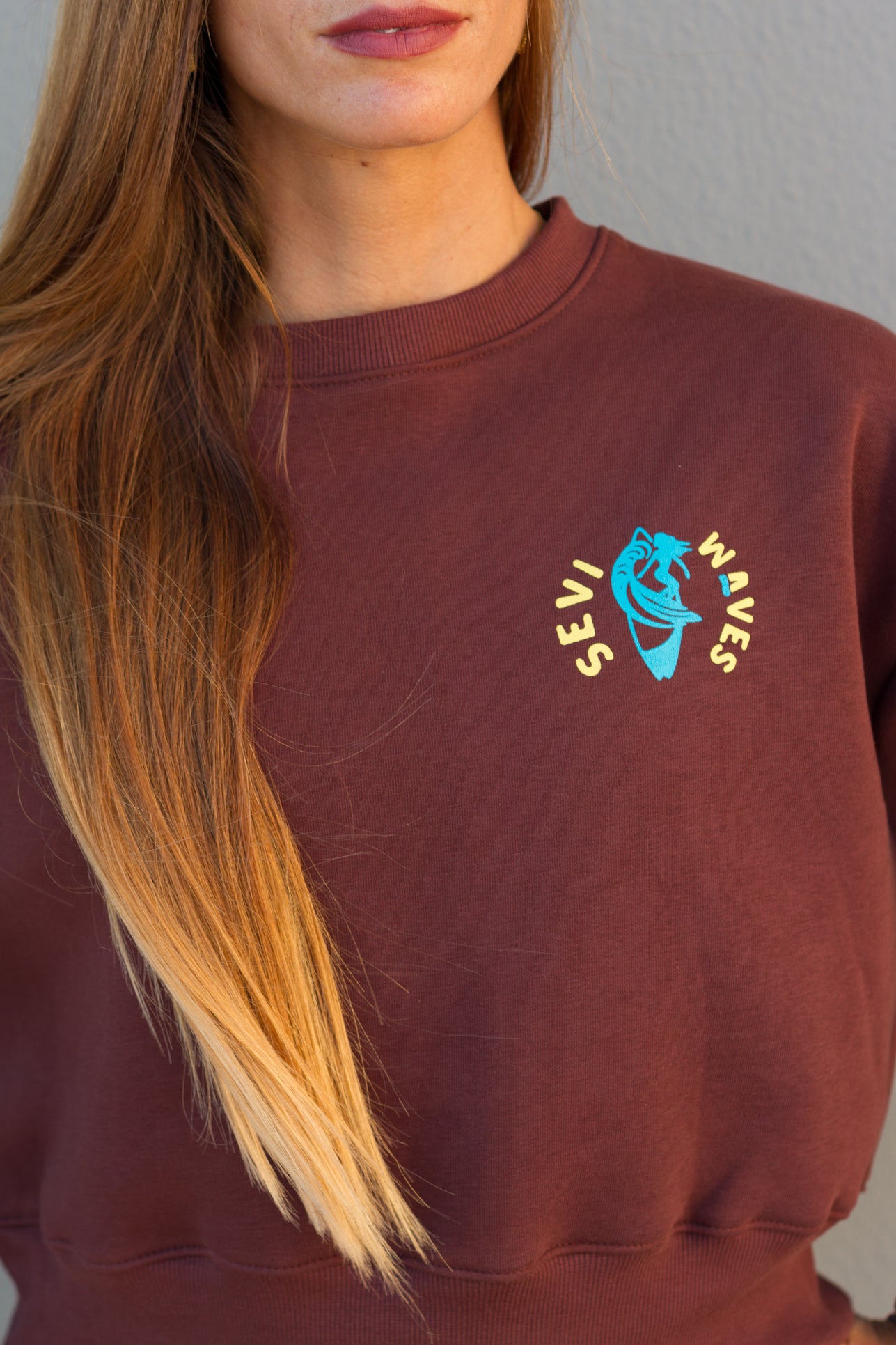 Maroon sweatshirt with a logo worn by a person with long blonde hair.