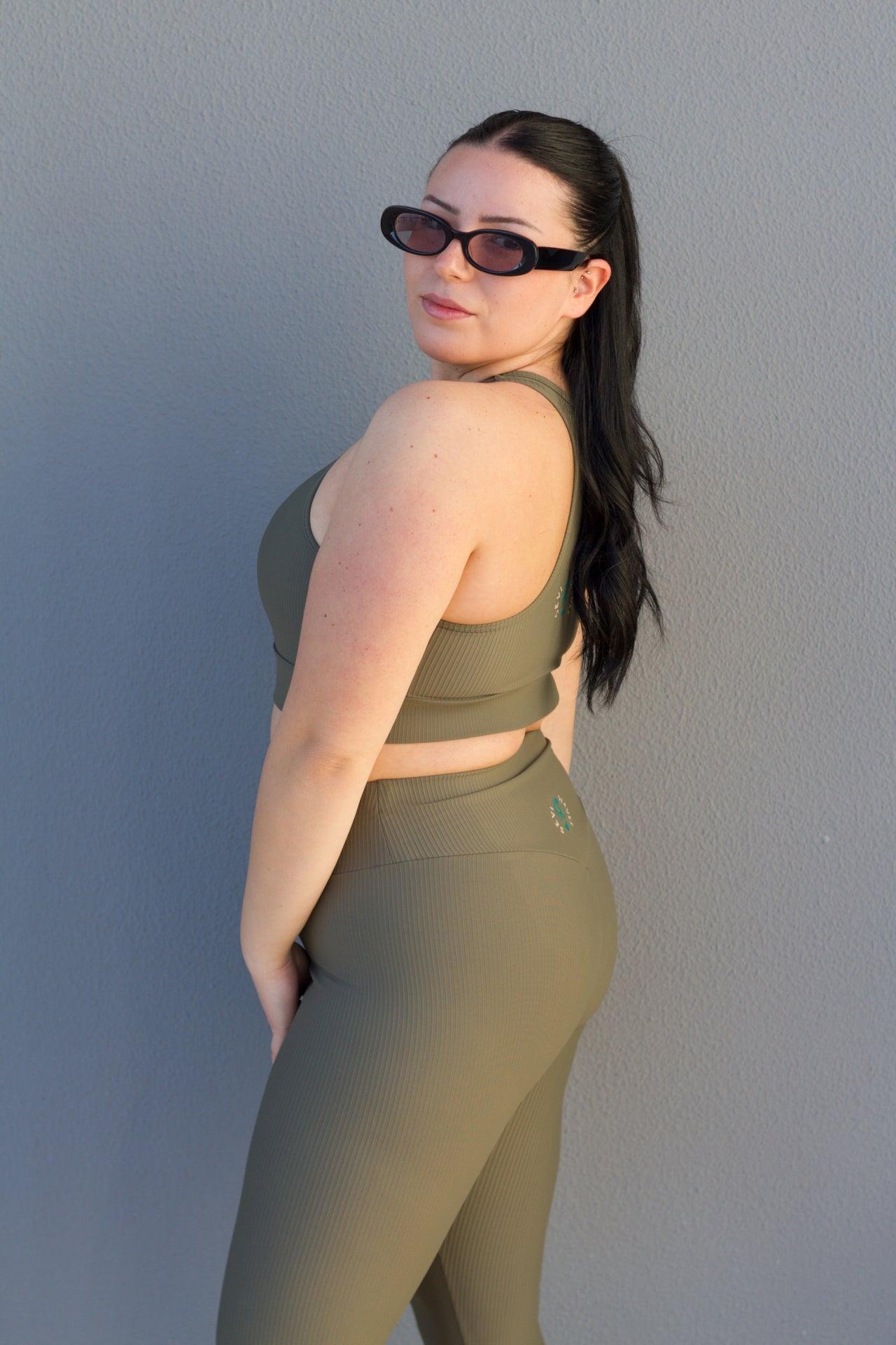 Woman wearing a green sports bra and leggings set against a gray wall.