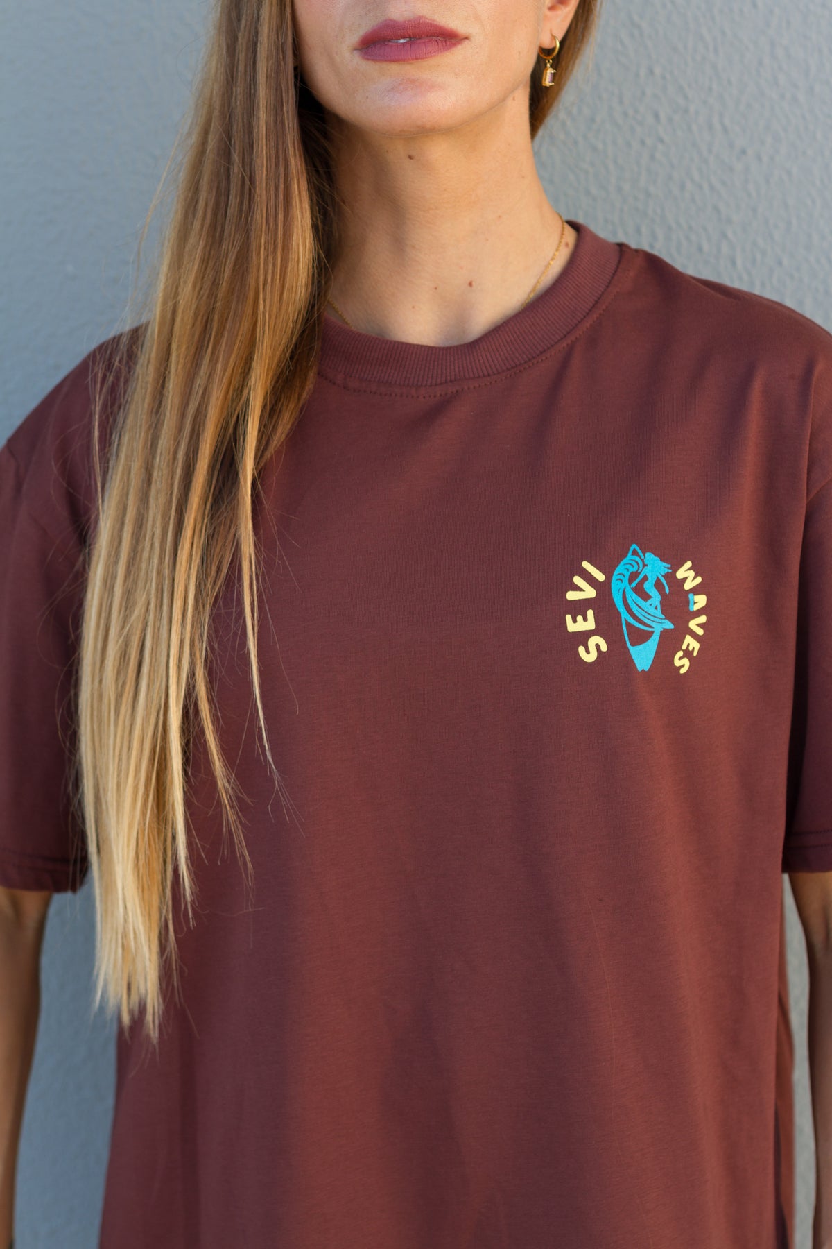 Person wearing a maroon t-shirt with a logo on a plain background