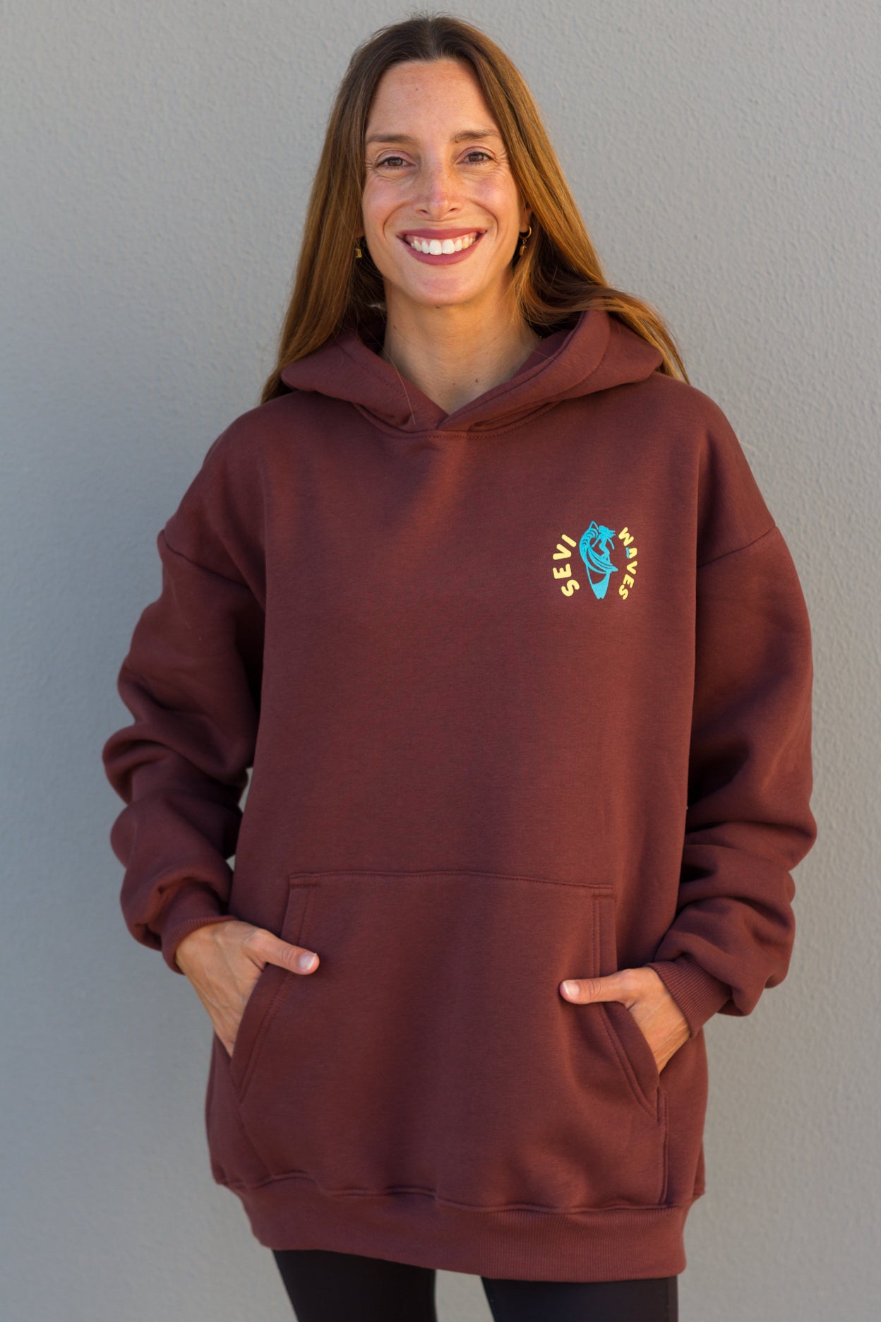 Woman wearing a maroon hoodie with a colorful logo against a gray background