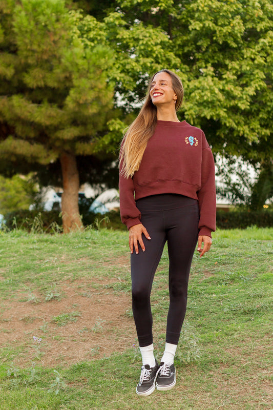 Woman wearing a maroon sweatshirt and black leggings standing in a park.