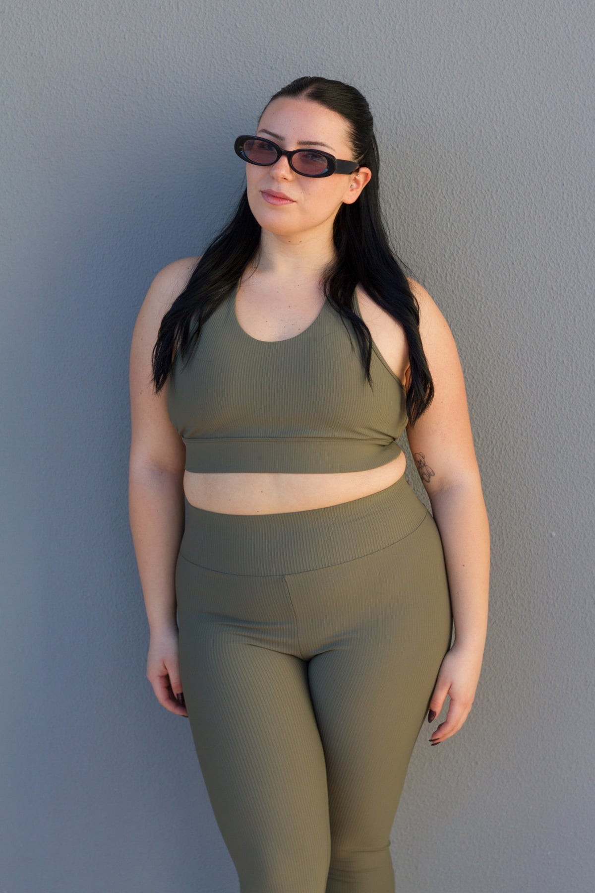 Woman wearing an olive green athletic outfit against a gray wall