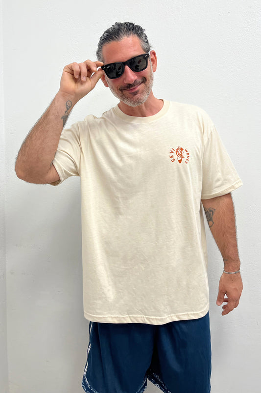 Man wearing a beige t-shirt with a logo and dark sunglasses against a white background