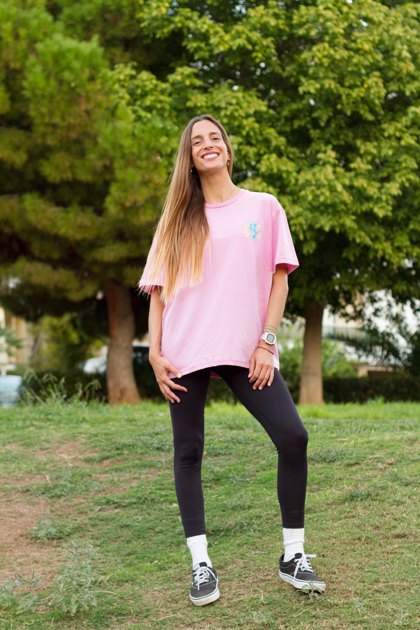 Woman wearing a pink oversized t-shirt and black leggings standing in a park.