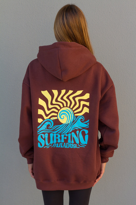 Person wearing a maroon hoodie with a colorful 'Surfing Paradise' design on the back against a plain background.