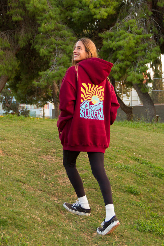 Person wearing a red hoodie with a graphic design, standing on grass with trees in the background