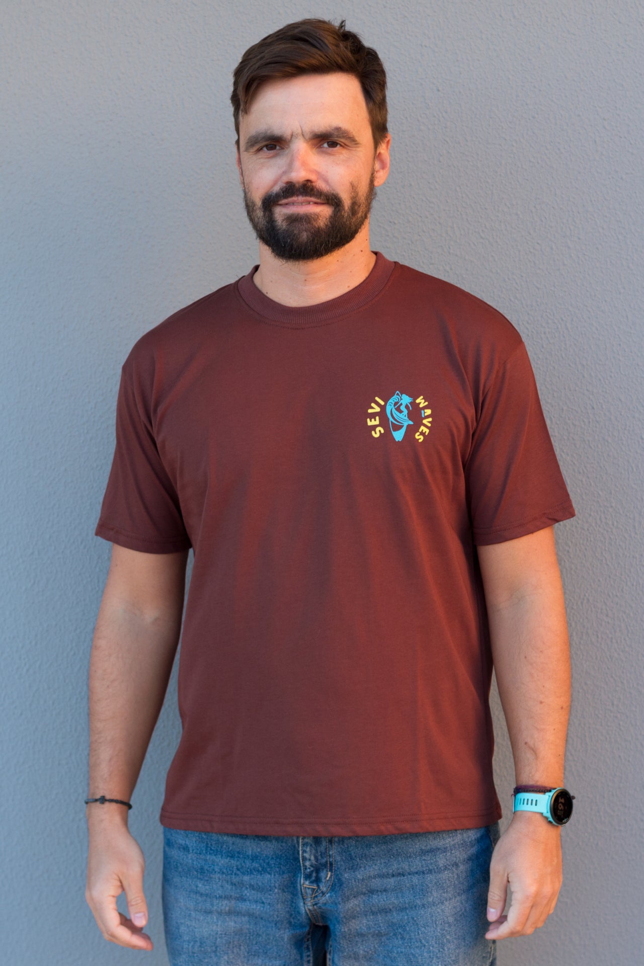 Man wearing a maroon t-shirt with a custom logo Sevi Waves against a gray background