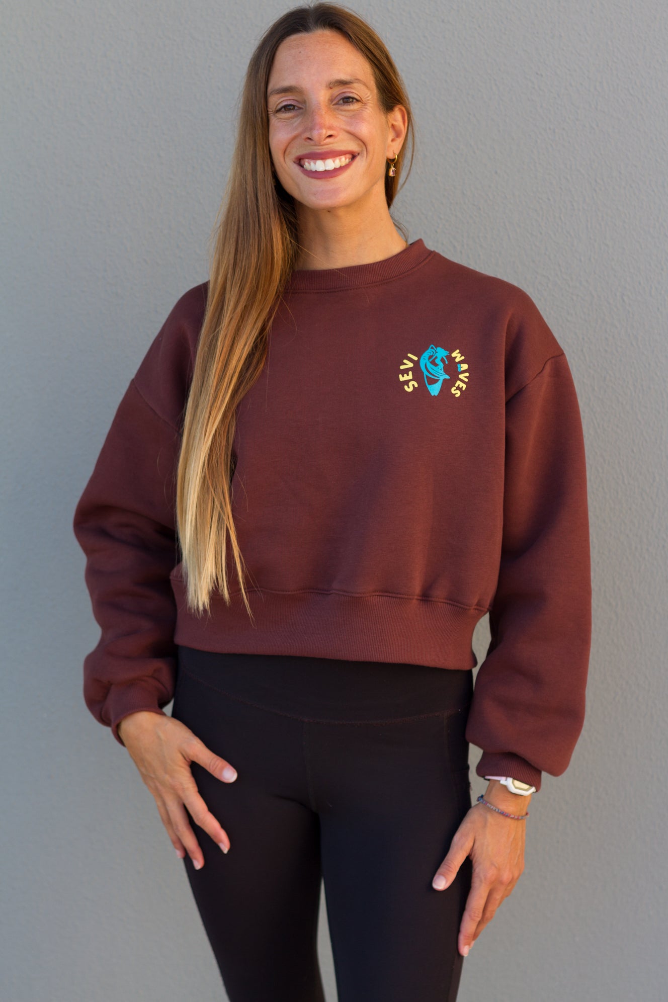 Woman wearing a maroon sweatshirt with a logo against a gray background
