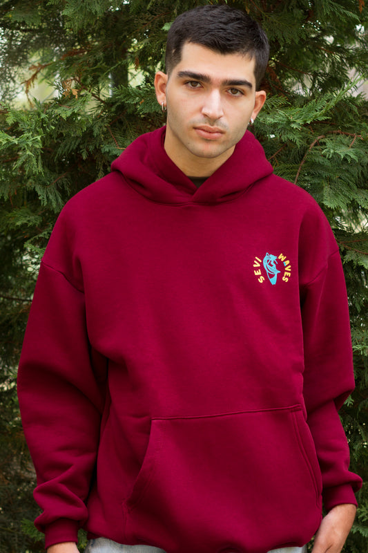 Person wearing a red hoodie with a logo in front of green trees