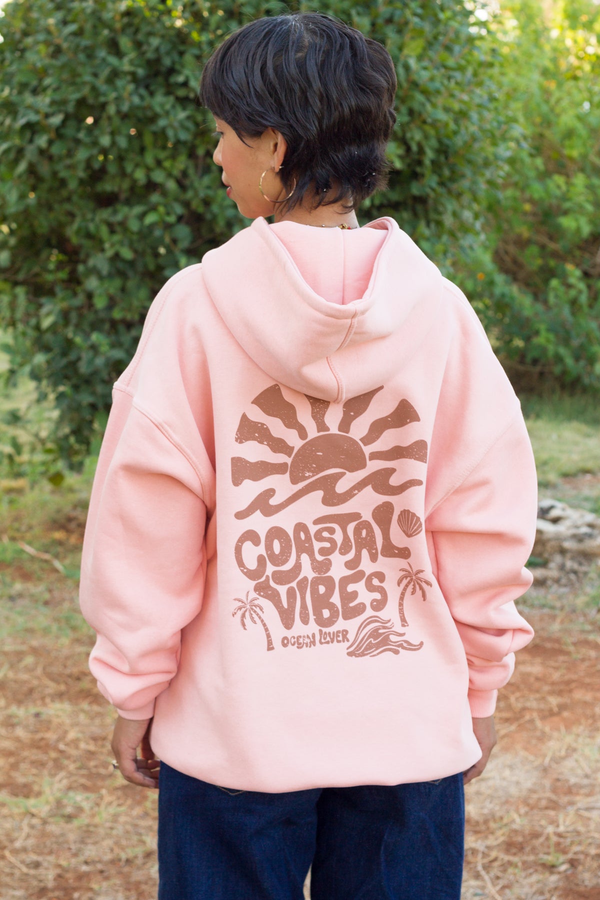 Back view of the salmon TIDE SHIFT hoodie featuring a vintage-inspired palms and shells illustration.