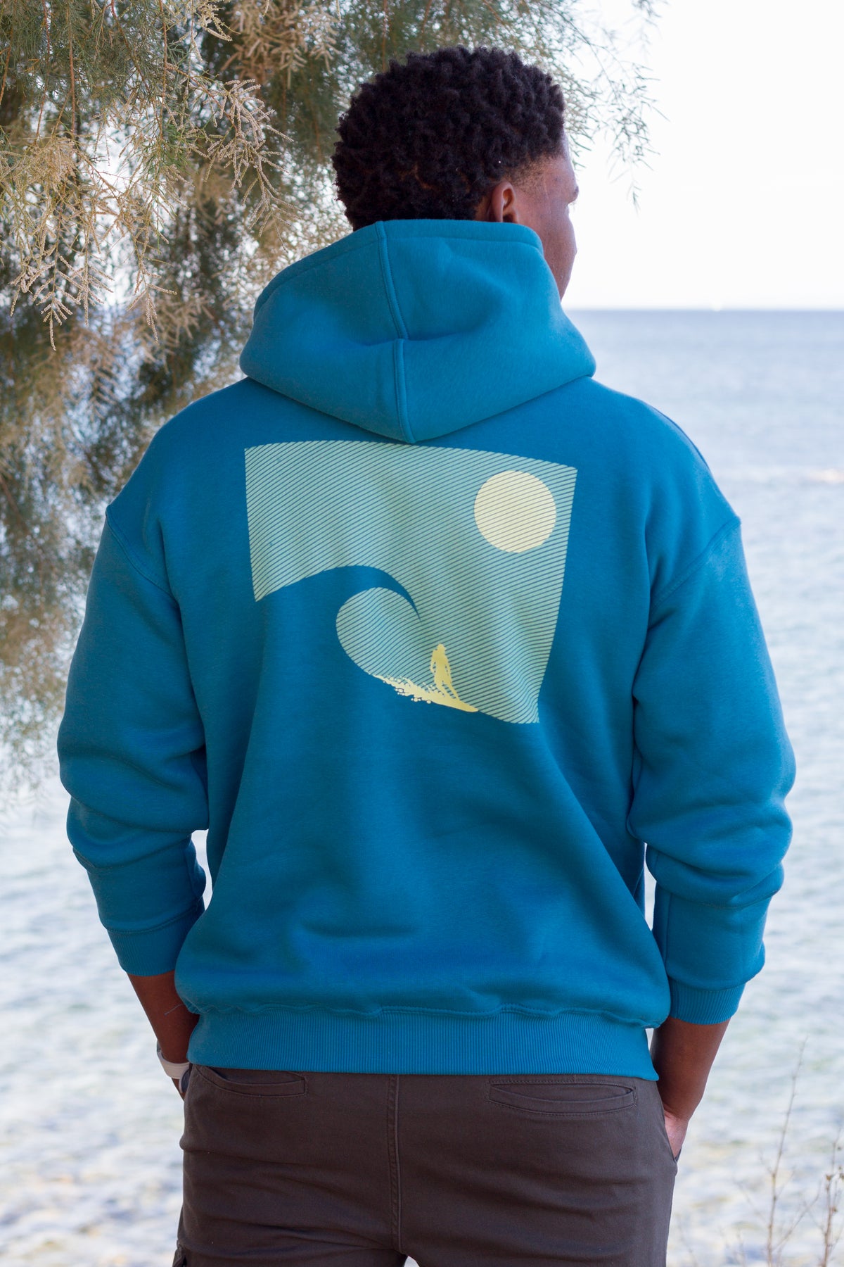 Back detail of a petrol Sevi Waves hoodie with a surf-inspired sunset and ocean print.