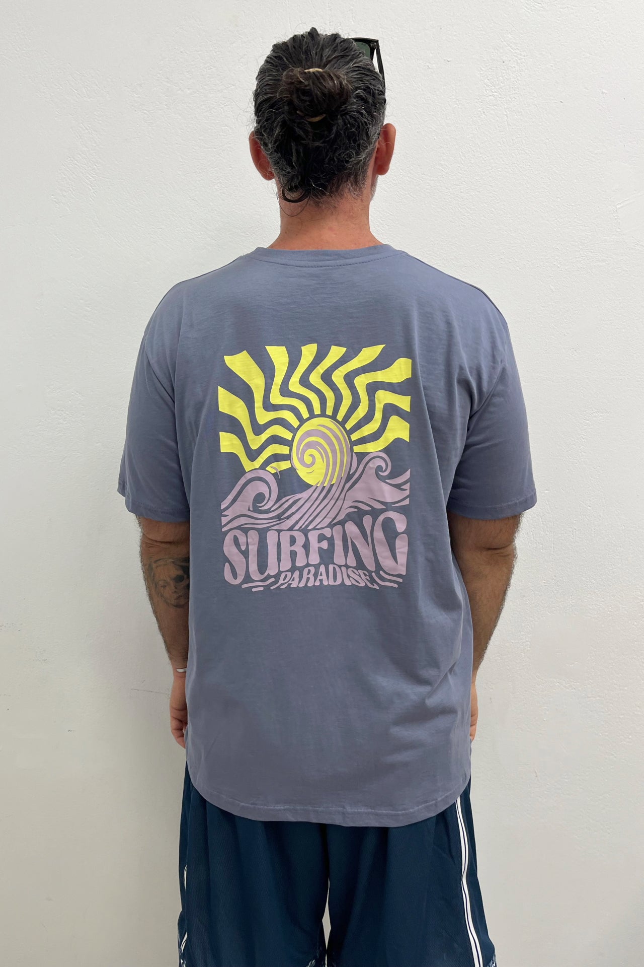 Person wearing a gray t-shirt with a yellow and purple 'Surfing Paradise' design on the back.
