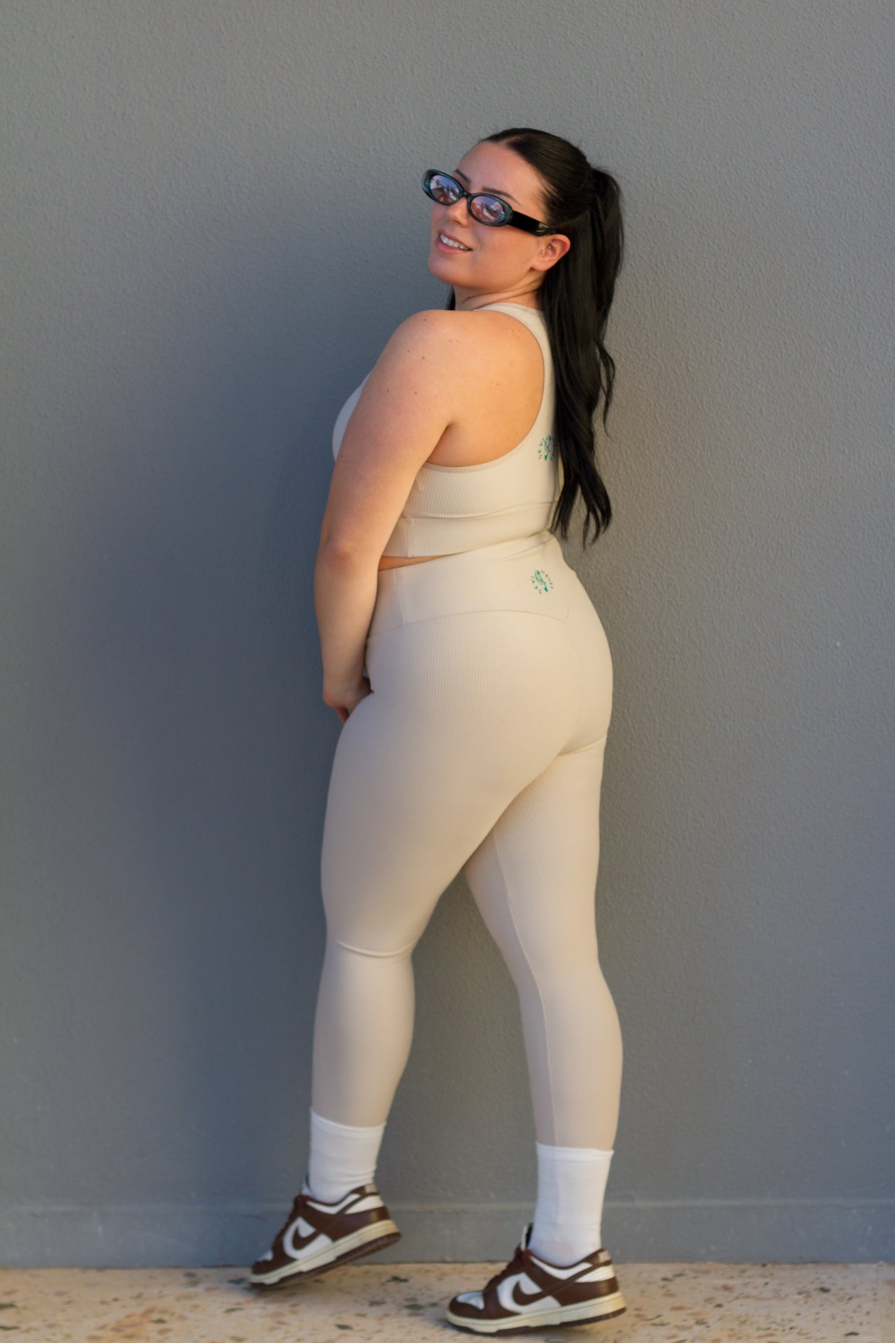 Woman wearing a beige athletic outfit against a gray wall