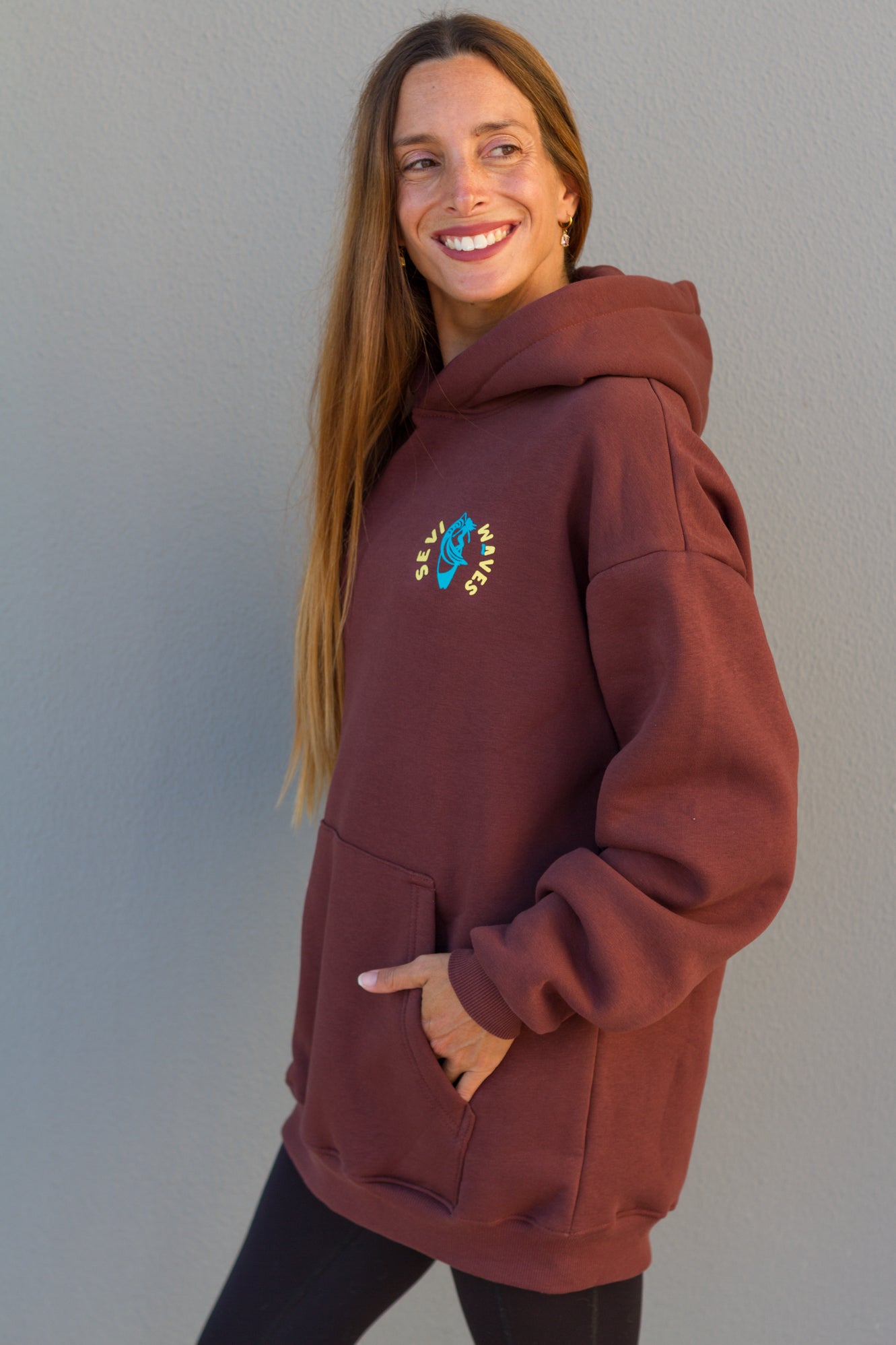 Woman wearing a maroon hoodie with a logo against a gray background