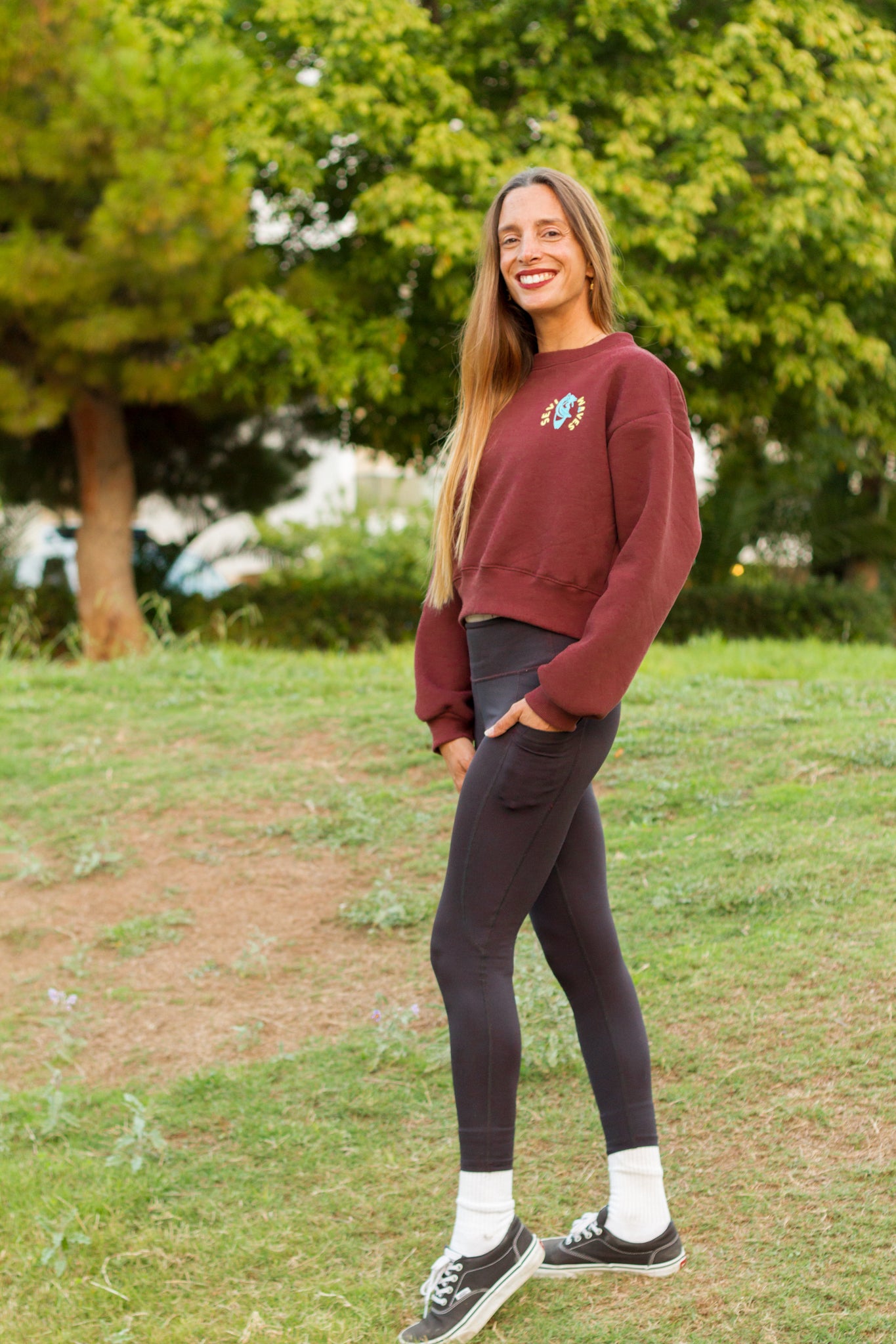 Woman wearing a burgundy sweatshirt and dark leggings standing in a park.