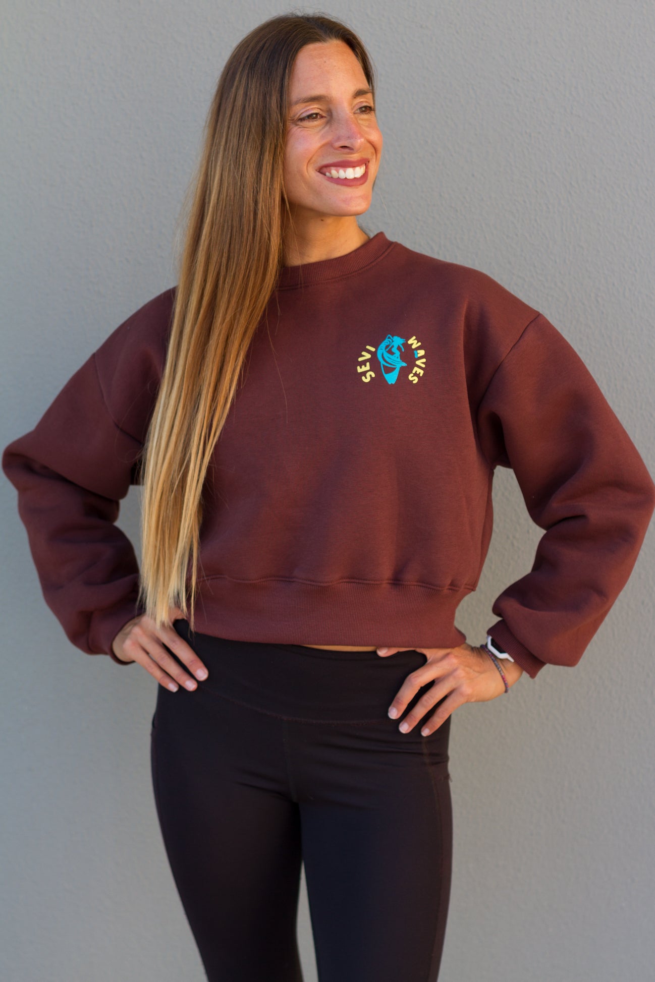 Woman wearing a maroon sweatshirt with a logo against a gray background