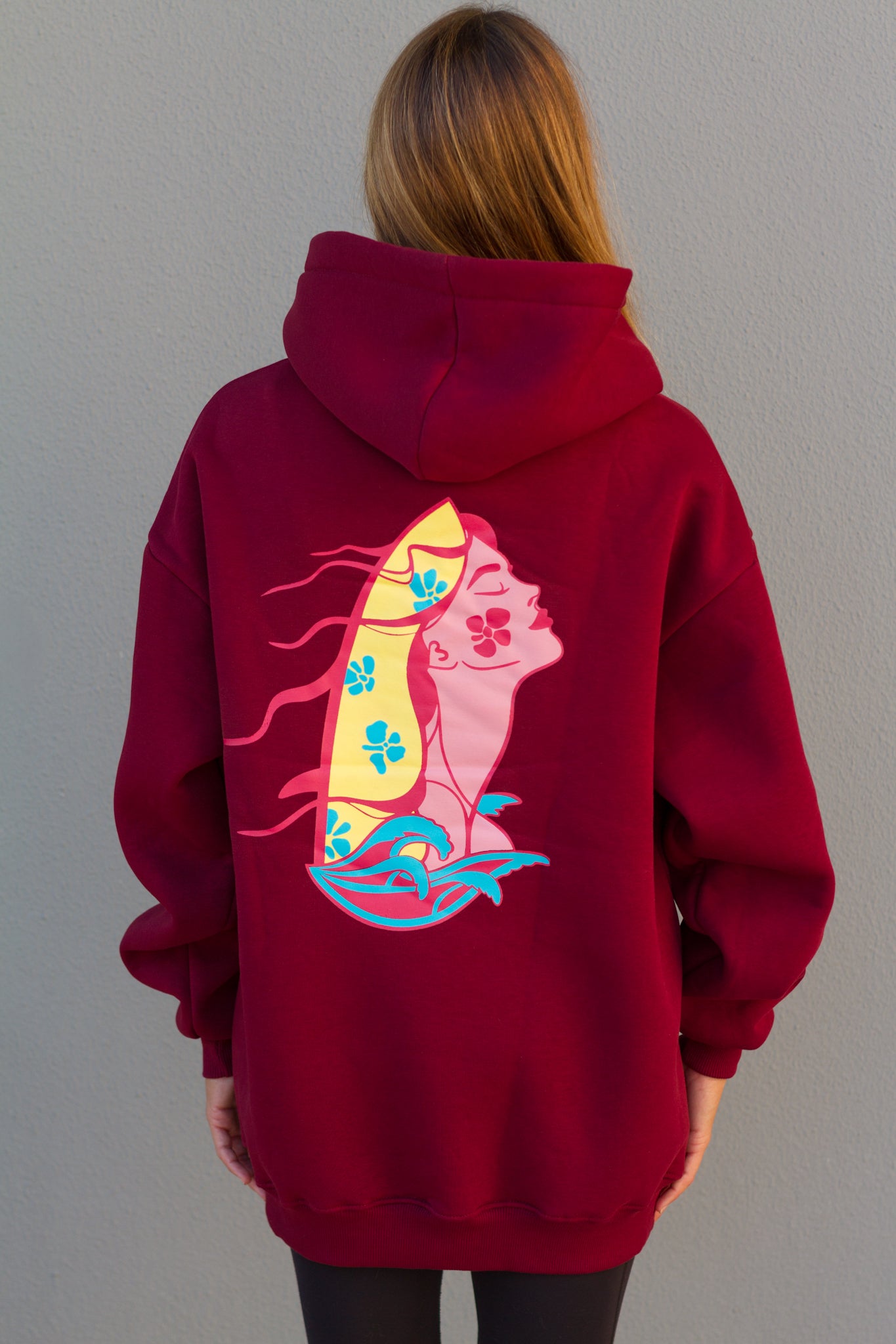 Person wearing a red hoodie with a colorful graphic on the back against a plain background