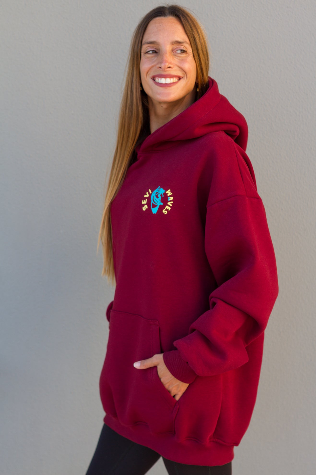 Woman wearing a red hoodie with a colorful logo against a plain background