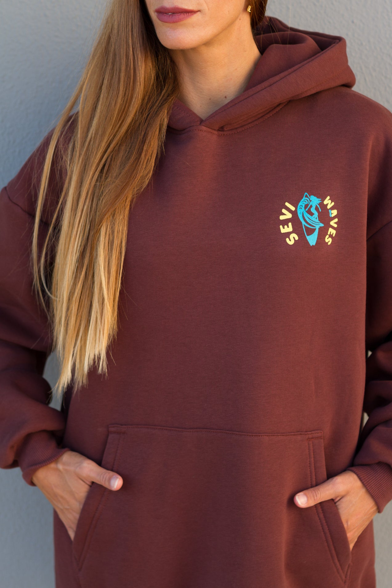 Person wearing a maroon hoodie with a logo on a plain background