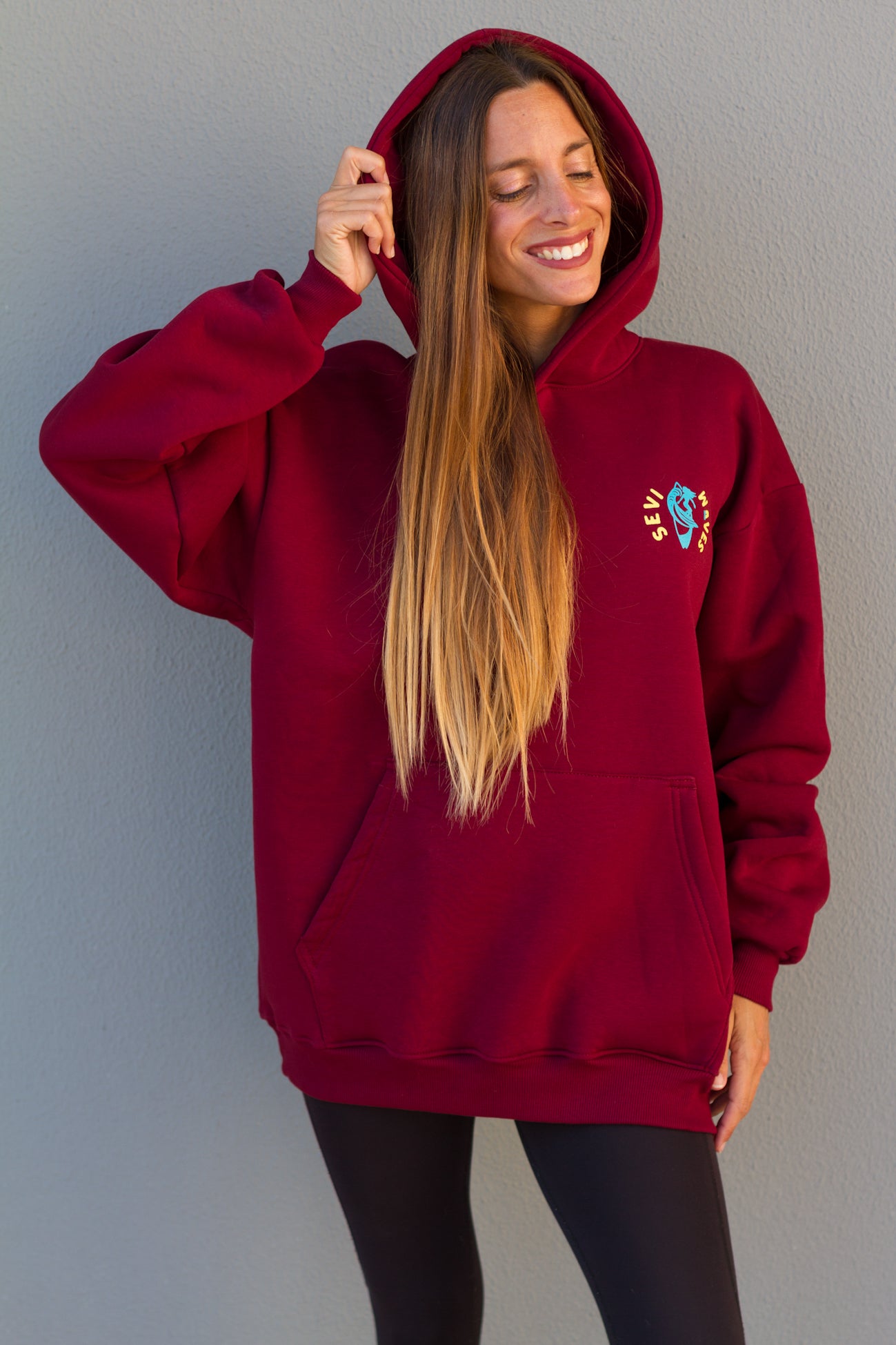 Woman wearing a red hoodie with a logo against a gray wall