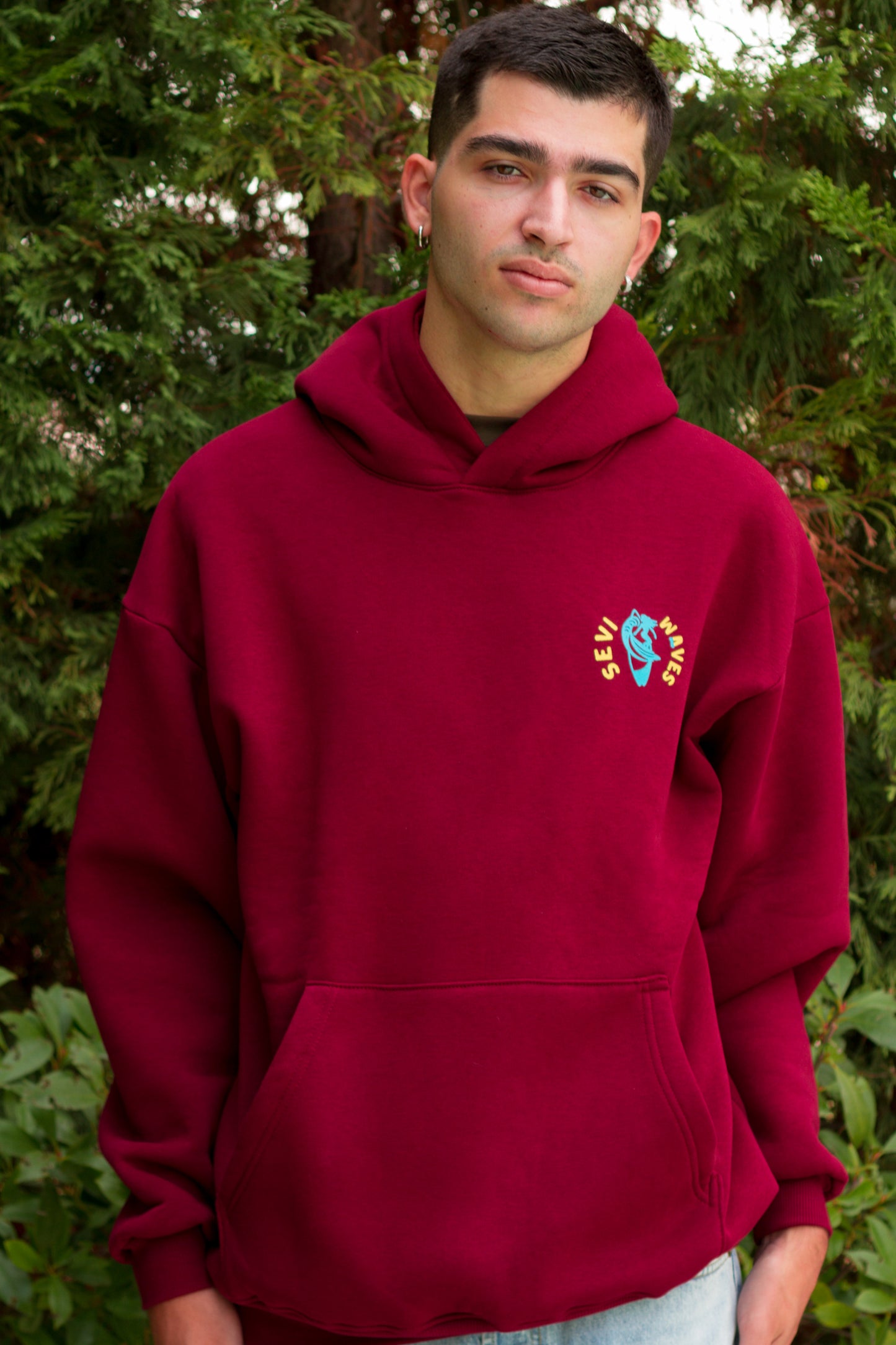 Man wearing a maroon hoodie with a colorful logo outdoors