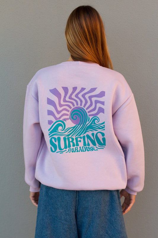 Person wearing a light purple sweatshirt with a 'Surfing Paradise' design on the back against a gray background