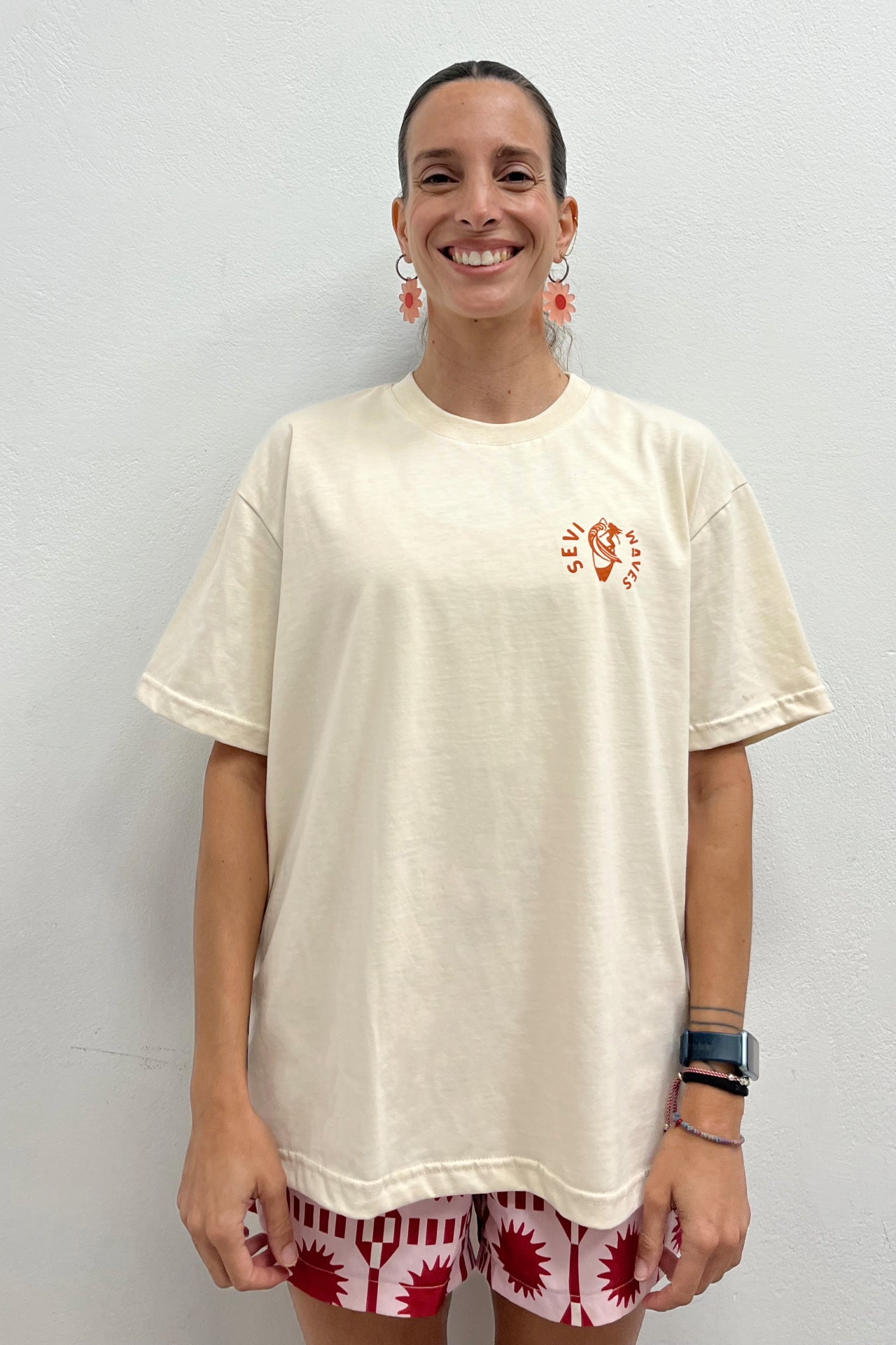 Person wearing a beige t-shirt with a logo and patterned shorts against a white background