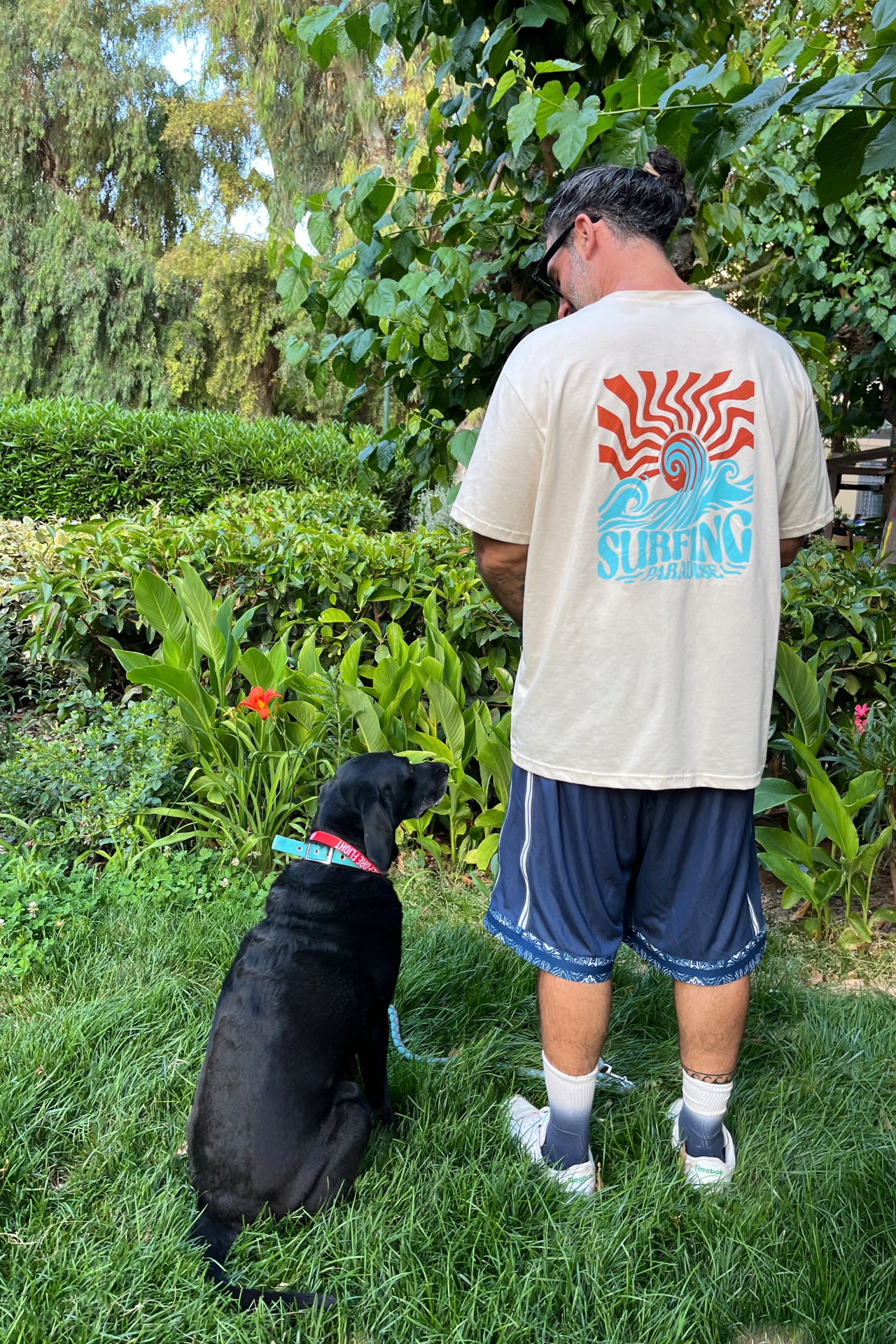 Man and black dog standing on grass with a garden background