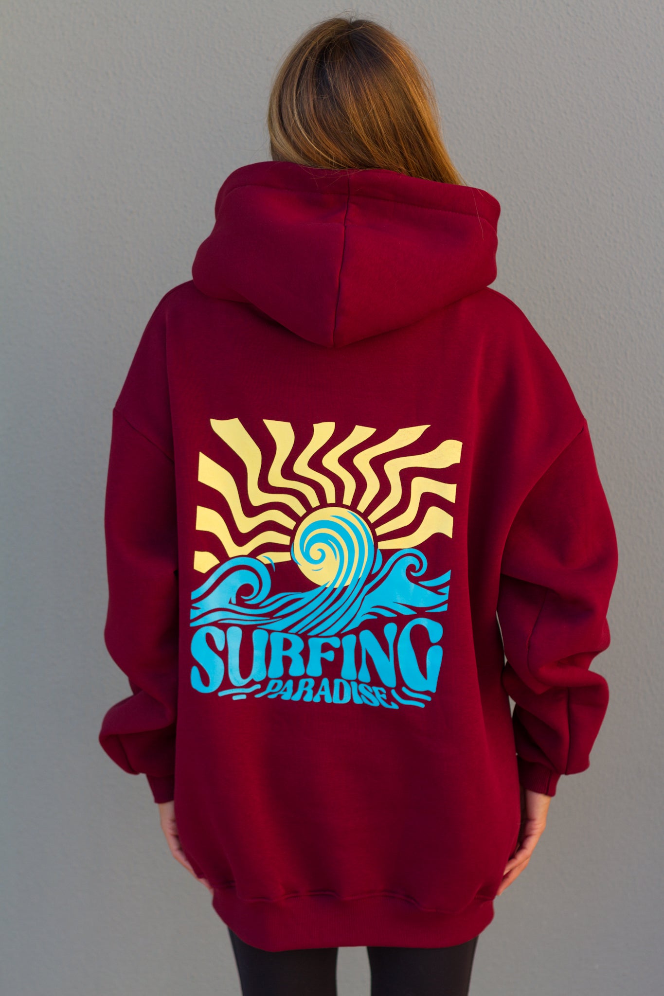Red hoodie with a 'Surfing' design on the back worn by a person against a plain background