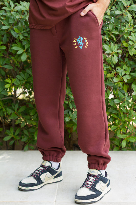 Maroon sweatpants with a colorful logo worn by a person, standing outdoors.